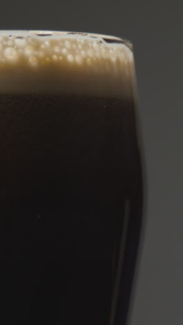 Vertical-Video-Close-Up-Of-Pint-Of-Irish-Stout-In-Glass-Against-Black-Background-To-Celebrate-St-Patricks-Day-2